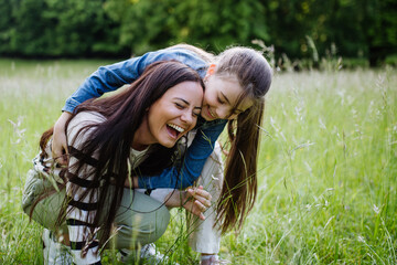 Beautiful mother with daughter, playing at meadow, piggybacking, having fun. Concept of Mother's...