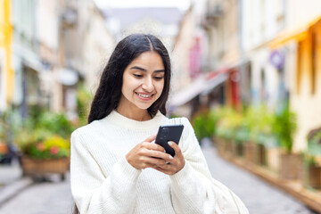 A young Indian girl walks on the city street and uses a mobile phone, calls, waits for an appointment, makes an online payment, rents in booking. Close-up photo