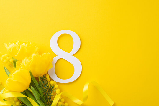 Joyful Women's Day design. Top view shot of a lavish bunch of tulips and mimosa, tied with a lace, and an 8 figure, against a brilliant yellow background with blank space for wording