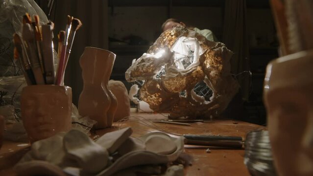 Stab shot of young female sculptor with flashlight in hands working on piece of art on work desk at night in dark workshopStab shot of young female sculptor with flashlight in hands working on piece o
