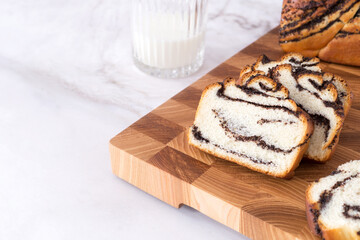 Festive poppy seed roll on wooden board with glass of milk. Fresh sweet bun, white background, homemade pastry