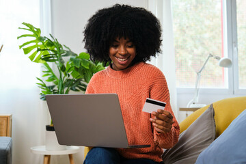 Cuban young woman buying online with a credit card in her laptop at home. Black Friday sales.