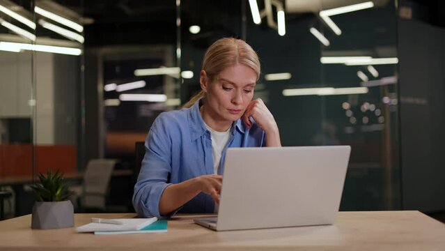 Young woman in casual outfit sitting at desktop and typing on laptop while getting annoyed with difficult task. Nervous female feeling bored while working on computer and sending emails to customers.