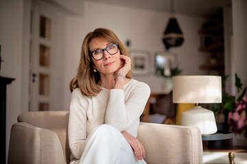Attractive mid aged woman sitting in her modern home and relaxing in an armchair