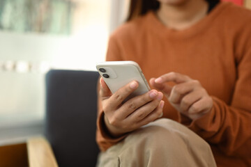 Closeup view young woman texting or chatting on mobile phone while relaxing at home