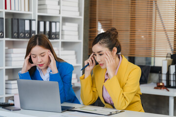 Two focused young Asian businesswomen or female accountants are discussing work, examining...