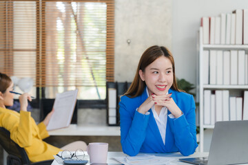 Two focused young Asian businesswomen or female accountants are discussing work, examining...