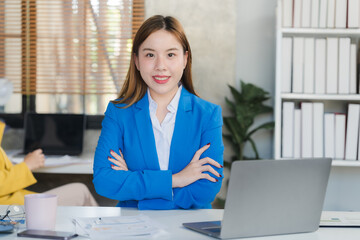 Two focused young Asian businesswomen or female accountants are discussing work, examining financial data, and working on reports in the office together.