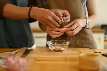 Hands of young couple peeling garlic on wooden chopping board. Healthy lifestyle concept