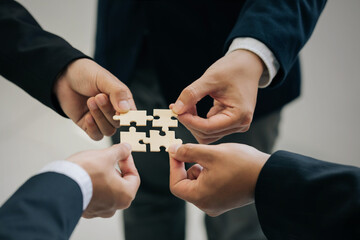 Concept of teamwork and partnership. Hands of business people join puzzle pieces together in the...