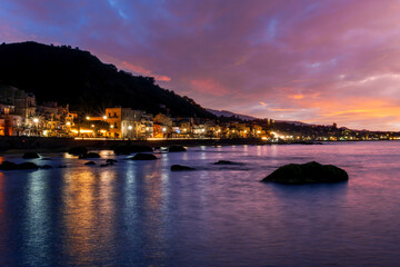 Fototapeta premium evening or night landscape of evening town coastline in golden lights and sea gulf with calm water and nice reflections with beautisul sunset sky on background
