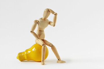 Wooden mannequin in thinking pose sitting on yellow light bulb - Concept of ideas and creative thinking
