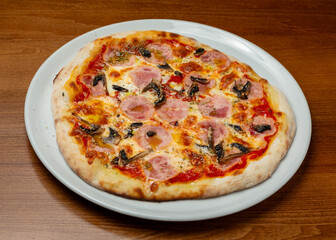 Italian pizza with ham and mushrooms on a plate.