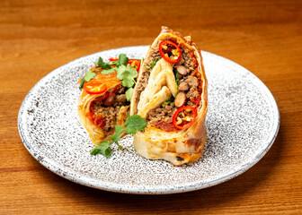 Mexican burrito dish with meat, beans and vegetables on a plate.