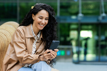 Professional young Hispanic businesswoman enjoying a break outside an office building, happily...