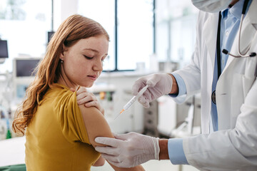 Doctor, pediatrician injecting vaccine into teenage girl arm. Concept of preventive health care and...