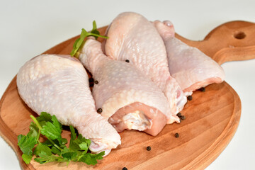 Three chicken legs lie on a cutting board, ready to be cooked.