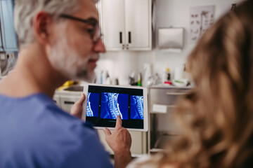 Doctor showing female patient MRI scan on tablet, discussing test result in emergency room.
