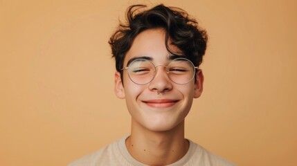 Young person with curly hair wearing glasses and a septum piercing smiling against a warm orange background. - obrazy, fototapety, plakaty