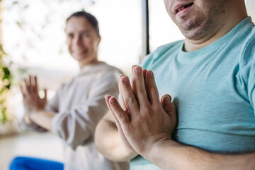 Obraz premium Young man with Down syndrome exercising at home with his mother, sitting on gym mat. Workout routine for disabled man.