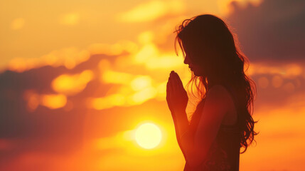 Young woman praying on the background of the setting sun
