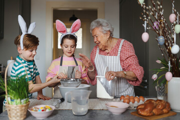 Grandmother with grandchildren preparing traditional easter meals, baking cakes and sweets. Passing...