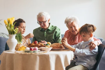 Fotobehang Grandparents with grandchildren eating traditional easter lunch. Recreating family traditions and customs. Happy easter. © Halfpoint