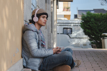 young man with headphones and phone sitting on the street