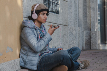 young man with headphones and phone sending a voice or audio message sitting on the street