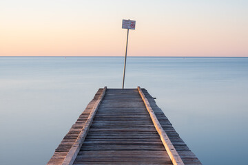 mystical photograph of a rustic pier leading into a calm sea at sunrise with a no jumping sign