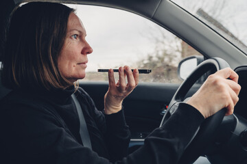 Woman driving car and talking on mobile phone while holding it in front of her mouth, communication...