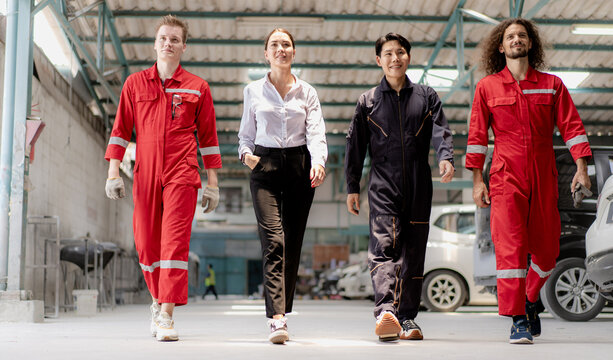 Auto mechanic team walking with smiling woman customer in repair garage ready to fix or maintenance damage engine cars parking in station shop. Diverse group of people at vehicle repair service shop.