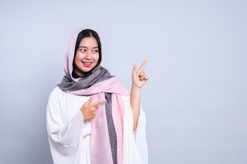 Cheerful Young Woman Wearing Veil Pointing Aside Over Gray Background. Eid and Ramadan Promotion...