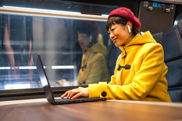 Beautiful Japanese woman working on laptop computer while commuting by train to work.