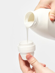 hand pours liquid conditioner powder into a cap white background