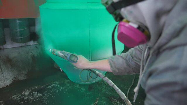 Painter spraying green paint on detail in special booth. Technician in safety wear working at industrial manufacturing. Painting process in chamber at factory. Man painting parts in production. Slowmo
