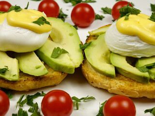 Eggs Benedict with fresh avocado placed on a plate with fresh cherry tomatoes, traditional breakfast 