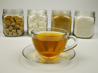 A glass cup of tea against the background of the glass jars with various types of sugar