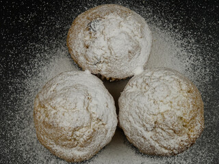 Freshly baked muffins with powdered sugar on a black plate