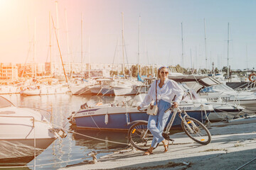 Woman enjoys bike ride along waterfront, Marina surroundings. She is wearing a white shirt and blue...