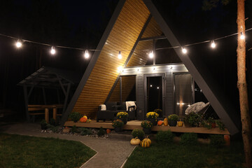 A-frame house in a pine forest. the a-frame house glows with garlands in the evening. rest in the...