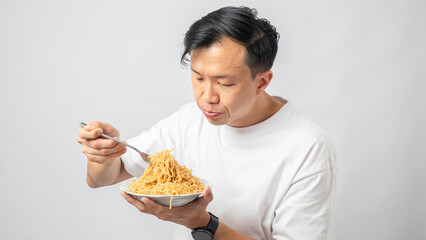 Portrait of an Indonesian Asian man, wearing a white T-shirt, enjoying eating noodles, isolated against a white background.