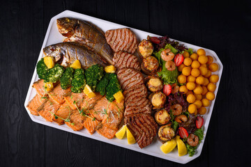 fried fish, fish steaks, shrimp, assorted. on a black wooden background