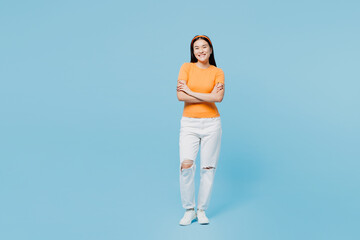 Fototapeta na wymiar Full body smiling happy young woman of Asian ethnicity she wear orange t-shirt casual clothes hold hands crossed folded isolated on pastel light blue cyan background studio portrait Lifestyle concept.