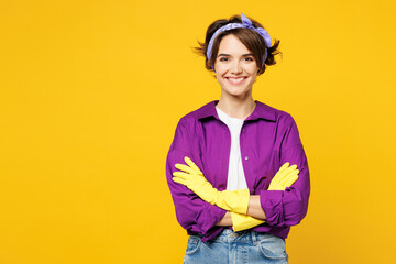 Young smiling happy cheerful woman she wear purple shirt rubber gloves while doing housework tidy up hold hands crossed folded isolated on plain yellow background studio portrait Housekeeping concept - obrazy, fototapety, plakaty