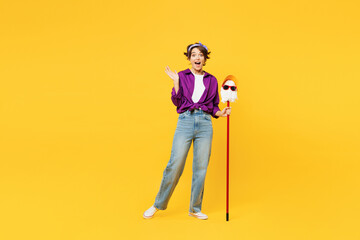 Full body young happy woman wear purple shirt casual clothes do housework tidy up hold in hand mop in hat and glasses kidding isolated on plain yellow background studio portrait. Housekeeping concept