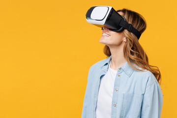 Young smiling happy amazed cheerful woman she wearing blue shirt white t-shirt casual clothes watching in vr headset pc gadget isolated on plain yellow background studio portrait. Lifestyle concept.