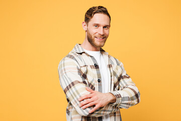 Side view young smiling happy fun Caucasian man he wear brown shirt casual clothes hold hands crossed folded look camera isolated on plain yellow orange background studio portrait. Lifestyle concept.