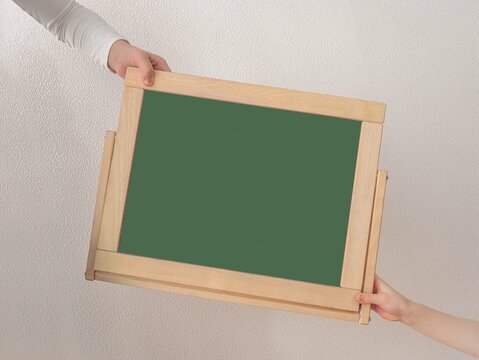 A Blackboard On A Green Background With A Place For Text Is Passed From The Hands Of Children. Back To School. Minimalism