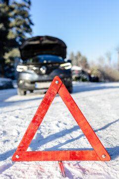 Broken car parked with a warning triangle in a snowy road.